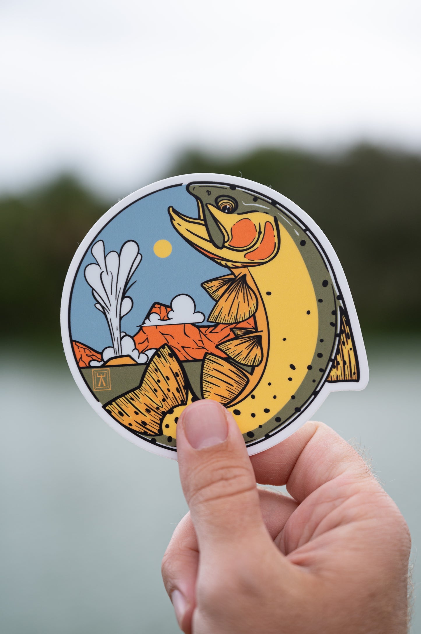 Hand holding circular sticker featuring a cutthroat trout